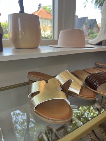 Slipper goud Elena met brede bandjes, op glazen tafel naast andere schoenen