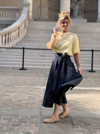 Willeke klokkende rok navy, gedragen met geel shirt en beige slippers, volledige outfit zicht op trappe