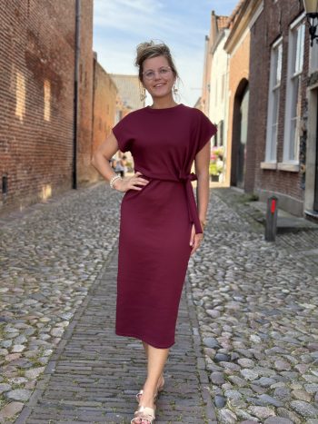 Mathilde jurk doorknoop roze, getragen door model in nauwe straatje met bakstenen huizen